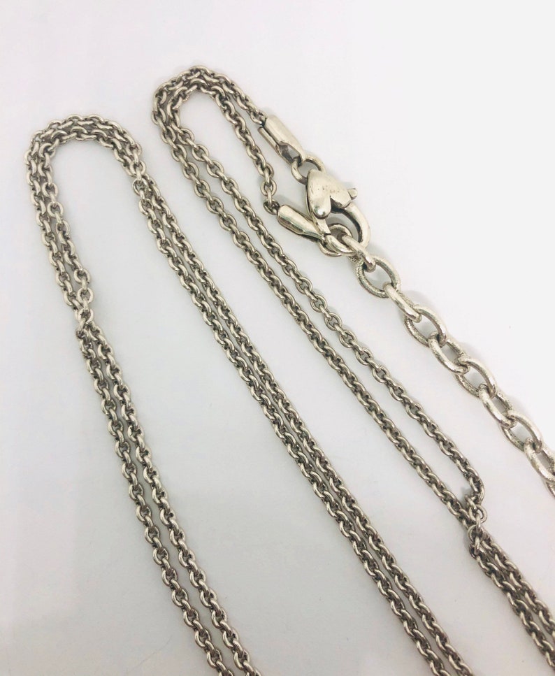 May include: Two silver chains with a heart-shaped clasp. The chains are of different lengths and thicknesses.