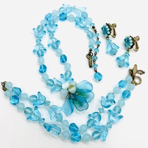 May include: A vintage blue glass necklace and earrings set with a flower pendant. The necklace is made of two strands of beads and the earrings are dangle style.