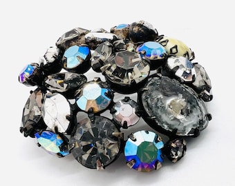 May include: A vintage brooch with a cluster of iridescent and clear rhinestones in a variety of shapes and sizes. The brooch is set in a silver tone metal.