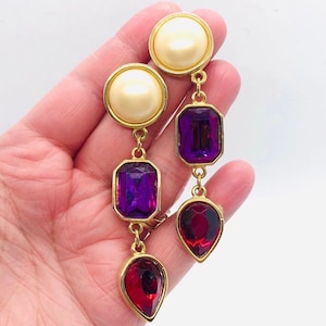 May include: Gold tone dangle earrings with a white pearl, a purple square gem, and a red teardrop gem.
