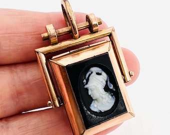 May include: A gold-toned locket with a hinged opening. The locket features a black cameo with a white portrait of a woman wearing a helmet.