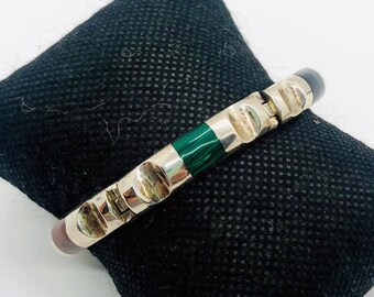 May include: A silver hinged bangle bracelet with green, black, and red stones.