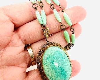 May include: A vintage green glass pendant necklace with a brass chain and oval-shaped pendant. The pendant has a detailed brass frame and a green glass stone.