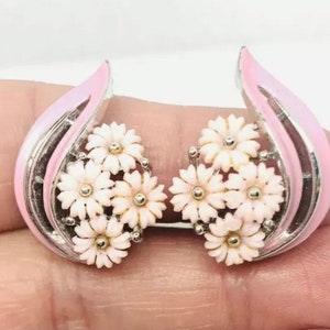 May include: A pair of pink and silver earrings with a cluster of white flowers. The earrings are shaped like a teardrop and have a delicate design.