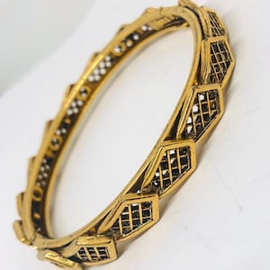 May include: A gold-toned bangle bracelet with a geometric design. The bracelet is made of metal and has a delicate, openwork pattern.