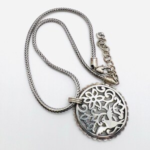 May include: A silver necklace with a round pendant featuring a delicate, cutout design of a bird and floral motifs.