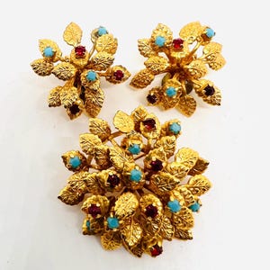 May include: A set of three gold-tone jewelry pieces featuring a cluster of leaves with turquoise and red stones.