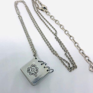 May include: A silver necklace featuring a silver charm in the shape of a small book with a four-leaf clover design. The chain is a delicate, double-strand chain.