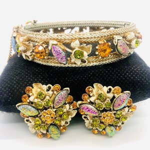 May include: A gold-tone bracelet with a floral design and iridescent stones. The bracelet is paired with matching earrings with a similar design.