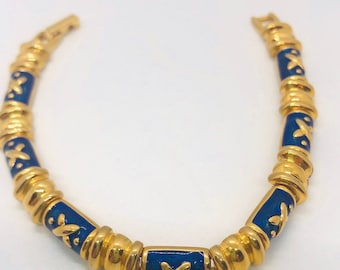 May include: A gold bracelet with blue enamel and a gold X pattern. The bracelet is made of small, round beads.