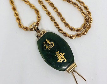 May include: A gold chain necklace with a green jade pendant. The pendant is oval shaped and has gold Chinese characters on it.