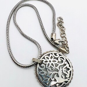 May include: A silver necklace with a delicate chain and a pendant featuring a circular design with a bird and floral motifs.