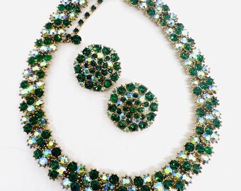 May include: A vintage jewelry set featuring a necklace and matching earrings. The set is adorned with emerald green and iridescent rhinestones set in a gold-tone metal. The necklace and earrings have a floral design.