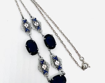 May include: Silver-toned necklace featuring oval, dark blue gemstones and decorative filigree elements. The filigree sections incorporate blue and white enamel accents, with a delicate chain and clasp.