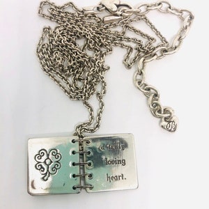 May include: Silver necklace with a charm that looks like a small book with a four-leaf clover on the front and the words "a truly loving heart" on the back.