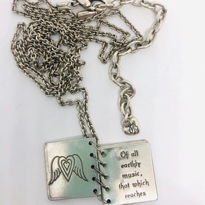 May include: A silver necklace with a charm that is a small book with wings and a heart on the front. The book is open and the inside says "Of all earthly music, that which reaches".