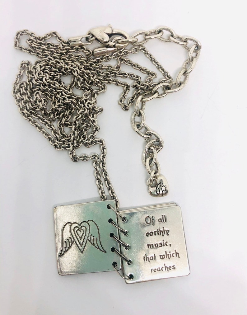 May include: A silver necklace with a charm that is a small book with wings and a heart on the front. The book is open and the inside says "Of all earthly music, that which reaches".