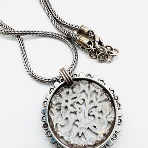May include: A silver necklace with a round pendant featuring a detailed, intricate design. The pendant is made of silver and has a delicate, filigree pattern.