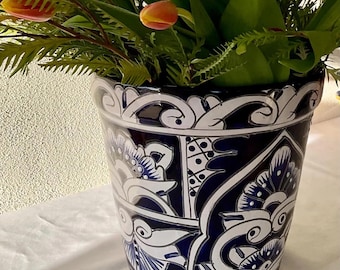 Puede incluir: Un macetero de cerámica azul y blanco con un diseño floral. El macetero está lleno de follaje verde y tulipanes naranjas.