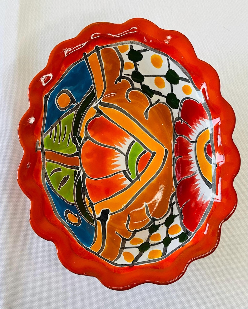 May include: A hand-painted, oval-shaped ceramic dish with a scalloped orange rim. The interior features a vibrant abstract design with orange, red, blue, green, and white colors. The dish is likely for decorative or serving purposes.