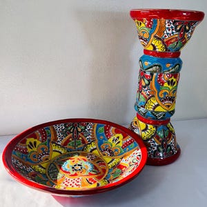 May include: A ceramic bowl and a tall cylindrical pedestal stand, both featuring a vibrant, multi-colored hand-painted floral and geometric pattern in shades of red, yellow, blue, green, and black with a glossy finish on the surfaces.