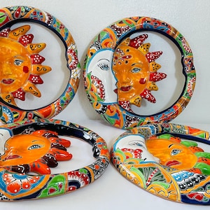 Puede incluir: Cuatro placas de pared circulares de cerámica con motivos de sol y luna. Cada pieza muestra una cara de sol naranja brillante con rayos y una cara de luna blanca de perfil, rodeadas por un borde colorido con patrones florales y geométricos.
