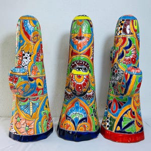 May include: Three tall, hand-painted ceramic sculptures with vibrant floral and geometric patterns in red, blue, yellow, and green. Each piece has a bulbous side element and a flared base, showcasing a unique, colorful design.
