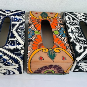 Op de afbeelding: Drie rechthoekige tissueboxhoezen met decoratieve ontwerpen. Eén is marineblauw en wit, een andere is bruin met oranje en groene bloempatronen, en de derde is zwart en wit. Elk heeft een ovale opening.