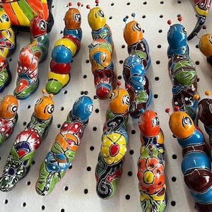 以下が含まれることがあります： カラフルな手描きセラミック製の毛虫のコレクション。各毛虫は、青、緑、黄、赤、オレンジなど、複雑な花柄と明るい色で飾られています。