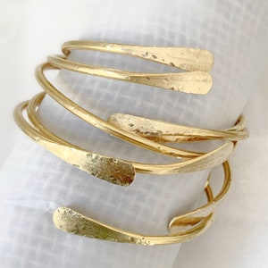 May include: A set of five gold-toned metal bangles with a hammered texture. The bangles are stacked on top of each other and have a slightly curved shape.