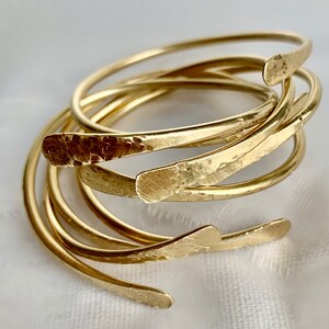 May include: A set of five gold-toned hammered metal bangles. The bangles are stacked on top of each other and have a slightly curved shape.