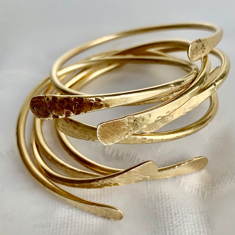 May include: A set of five gold-toned hammered metal bangles. The bangles are stacked on top of each other and have a slightly curved shape.