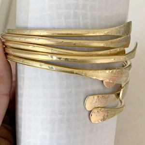 May include: A set of six gold-toned metal bangles with a hammered finish. The bangles are stacked on top of each other and have a slightly curved shape.