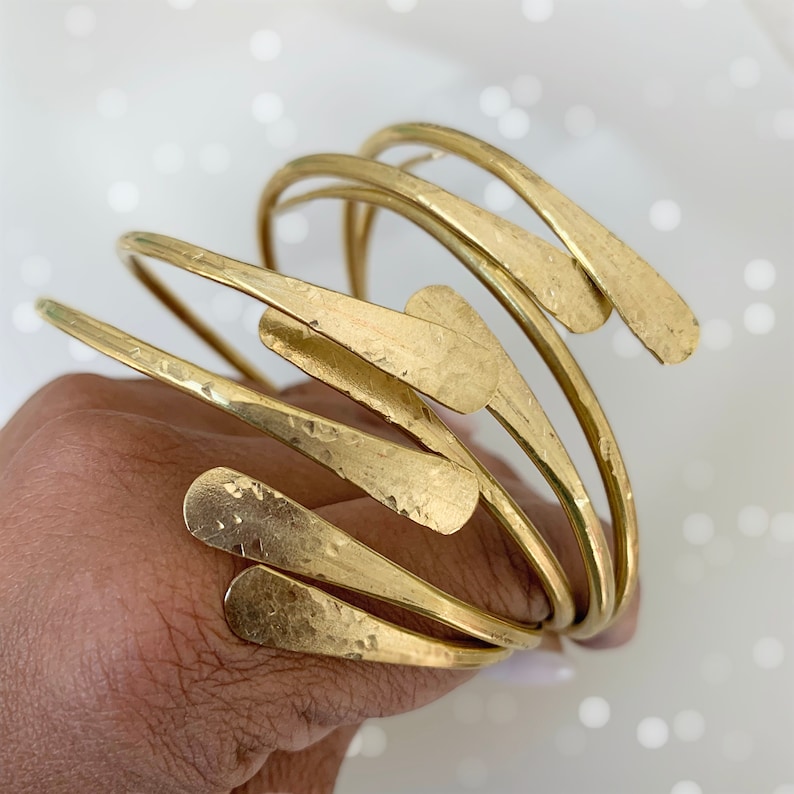 May include: A set of five gold-toned metal bangles with hammered texture and a unique teardrop shape at the end of each bangle.