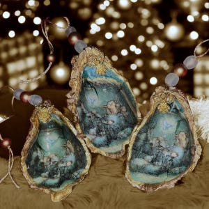May include: Three oyster shell ornaments with painted interior scenes, gold trim, and beaded hangers. The shells feature a blue and green color palette with a pastoral design. The ornaments are displayed on a soft, brown surface.