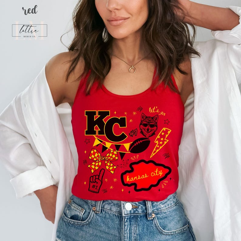May include: A red tank top with a graphic design featuring the letters "KC", a football, a wolf, and the words "Kansas City". The tank top also has a bow and a lightning bolt design.