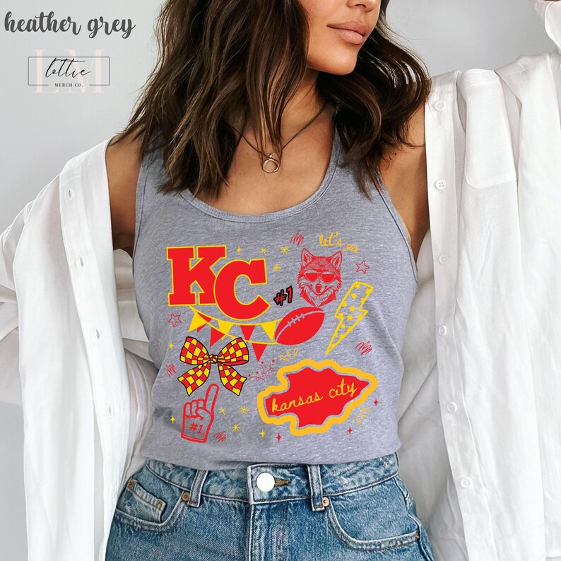 May include: Heather grey tank top with a red and yellow graphic design. The design includes the letters "KC", a football, a lightning bolt, a fox head, and the words "Kansas City". The tank top also has the text "#1".