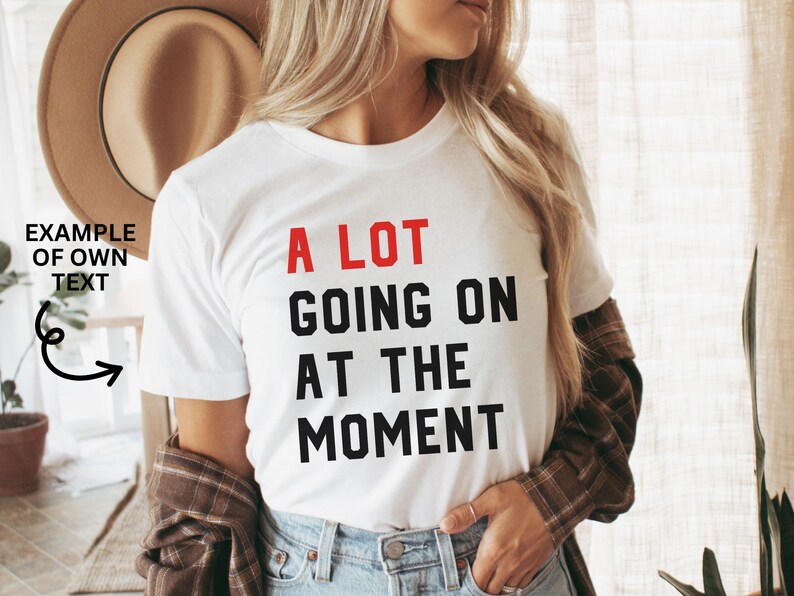 May include: White t-shirt with black text that reads "A LOT GOING ON AT THE MOMENT". The word "LOT" is in red.