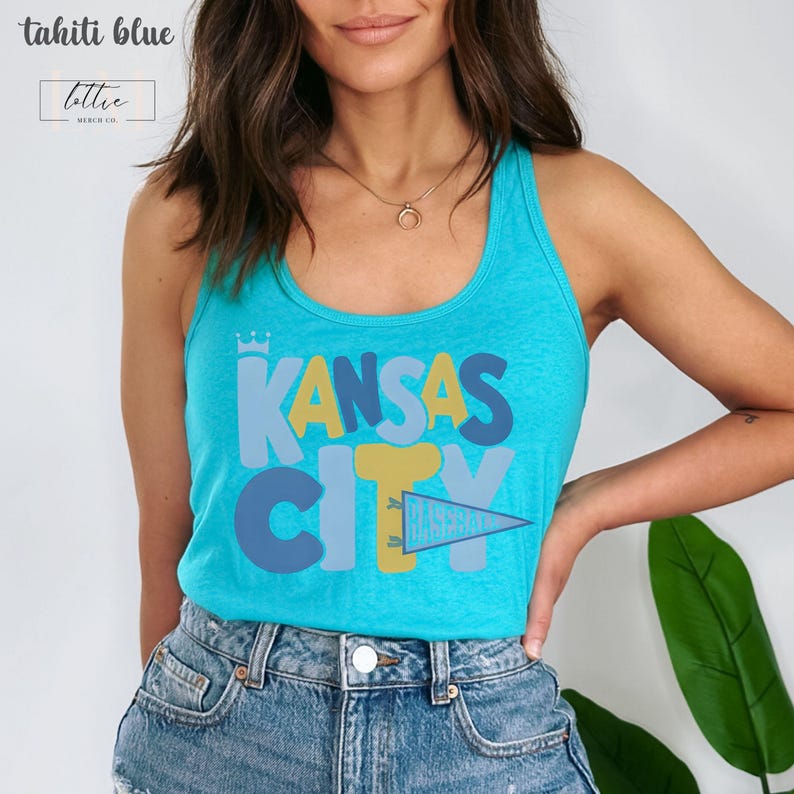 Op de afbeelding: Een turquoise tanktop met de woorden "KANSAS CITY" in een kleurrijk, speels lettertype. Het woord "CITY" wordt gedeeltelijk bedekt door een wimpel met de tekst "BASEBALL". De top is gelabeld "tahiti blue" en heeft een klein logo.