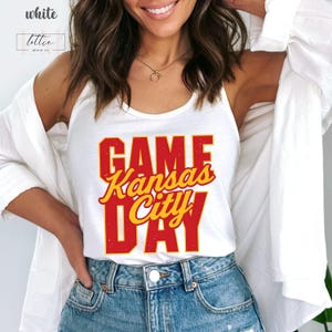 May include: White tank top with the text "GAME Kansas City DAY" in red and yellow lettering. The tank top is a casual style, perfect for game day or everyday wear. The shirt is made of a soft, comfortable material.