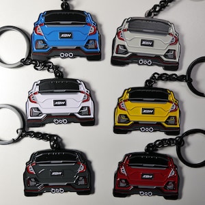 May include: A collection of six car keyrings in different colours: blue, white, yellow, black, grey, and red. Each keyring has a detailed car design with the text "XDM" and a black keyring. The keyrings are displayed together.