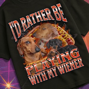 Puede incluir: Camiseta negra con la frase "I'd Rather Be Playing With My Wiener" en rojo y blanco, con ilustraciones de perros salchicha. La camiseta es parte de la colección "Mildly Perturbed", con un tema retro y espacial.