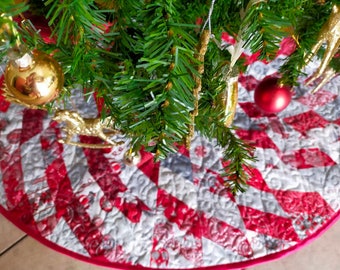 Puede incluir: Una falda de árbol de Navidad acolchada roja y blanca con un patrón en espiral. La falda tiene un borde rosa y está decorada con adornos dorados y un reno dorado.