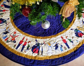 Puede incluir: Una falda de árbol de Navidad azul y dorada con un fondo blanco con temática de Cascanueces. La falda tiene un diseño acolchado y presenta una variedad de personajes de la historia de Cascanueces, incluido Cascanueces, la Hada de Azúcar y el Rey Ratón.
