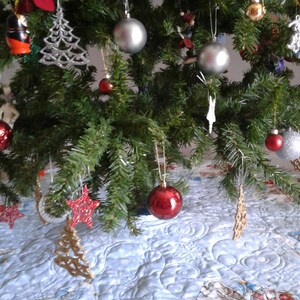 Puede incluir: Un &aacute;rbol de Navidad decorado con adornos plateados, estrellas rojas y doradas y un calcet&iacute;n rojo. El &aacute;rbol est&aacute; sobre una falda de &aacute;rbol acolchada azul claro con una escena invernal.
