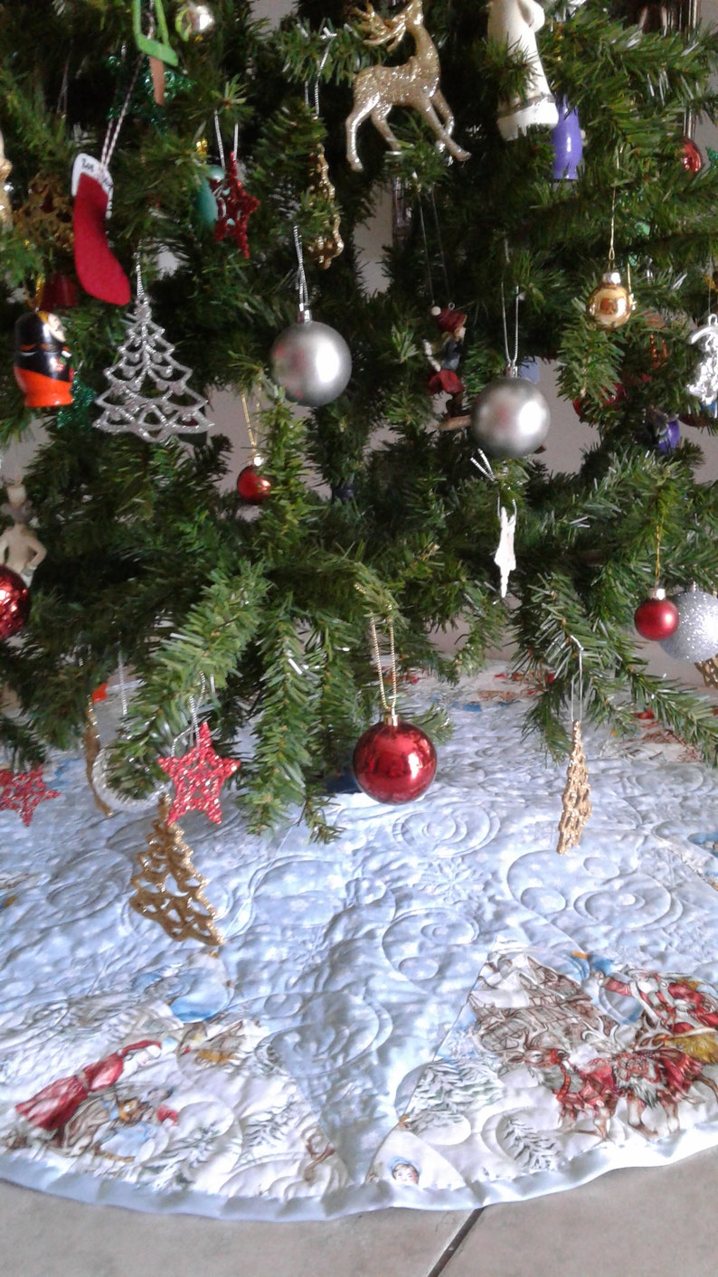 Puede incluir: Un &aacute;rbol de Navidad decorado con adornos plateados, estrellas rojas y doradas y un calcet&iacute;n rojo. El &aacute;rbol est&aacute; sobre una falda de &aacute;rbol acolchada azul claro con una escena invernal.