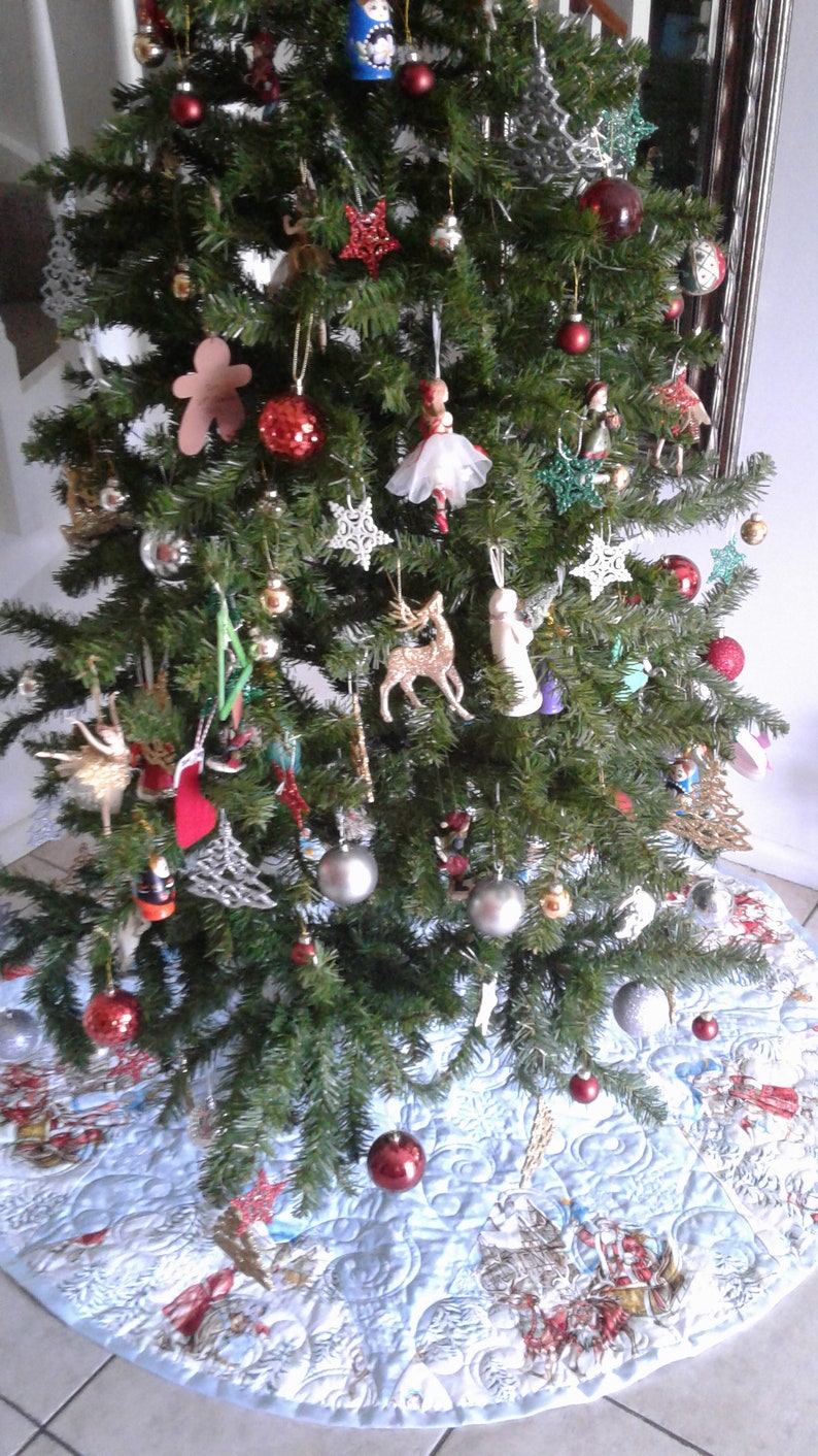 Puede incluir: Un &aacute;rbol de Navidad decorado con varios adornos, incluyendo bolas rojas y plateadas, decoraciones en forma de estrella y peque&ntilde;as figuras. El &aacute;rbol se encuentra sobre una falda de &aacute;rbol azul claro con un dise&ntilde;o de escena invernal.