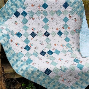 May include: A blue and white baby quilt with a patchwork design featuring a repeating pattern of rabbits and flowers. The quilt has a blue border with a white floral pattern.