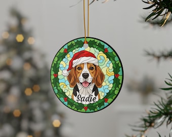 May include: Round Christmas ornament featuring a beagle wearing a Santa hat, surrounded by a green wreath with red berries. The dog's name, "Sadie," is written below. The ornament hangs from a gold string, perfect for holiday decor.