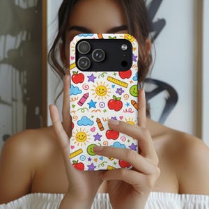 May include: A white smartphone case featuring a colorful pattern of school-themed icons including red apples, yellow suns with faces, blue clouds, purple stars, orange crayons, yellow rulers, and green smiley faces scattered across the surface.